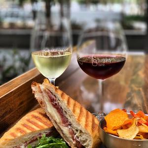 Glasses of red and white wine at a local wine bar. Gourmet sandwich with meat, cheese and side salad and homemade chips.